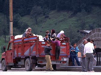 荷台に人も荷物も満載したトラックが山の村へ出発するところ