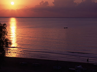 朝日で真っ赤に染まった地中海。漁に出ている小舟と散歩をする人影が見える。
